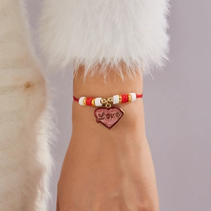 Detalle de pulsera con dije de corazón rojo y grabado 'Love' en cordón rojo trenzado