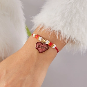Detalle de pulsera con colgante de corazón rojo, inscripción Love y cordón trenzado