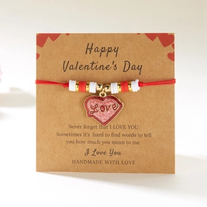 Detalle de la pulsera de cuerda trenzada roja con dije de corazón en tarjeta de San Valentín