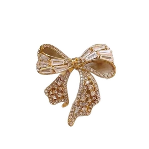 Broche nœud élégante en or ornée de strass blancs et de cristaux sur fond blanc épuré