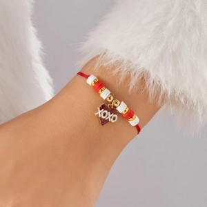 Detalle de una pulsera de cordón rojo con colgante de corazón XOXO y cuentas de arcilla de colores