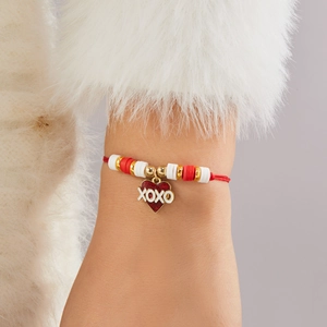 Detalle del dije de corazón rojo con texto XOXO en pulsera de cordón con cuentas doradas