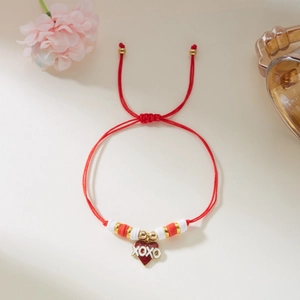Detalle de pulsera trenzada roja con colgante de corazón, texto XOXO y cuentas doradas