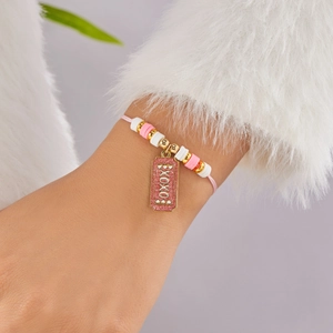 Detalle de pulsera de cuentas rosas y blancas con dije XOXO lucida sobre un suéter blanco
