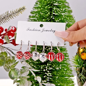 Trois paires de boucles d'oreilles boules de Noël avec motifs rouges sur carte blanche