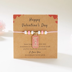Primer plano de pulsera artesanal con dije XOXO sobre tarjeta de regalo de San Valentín