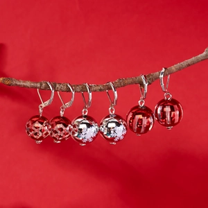 Détail de boucles d'oreilles boules de Noël rouges et argentées avec motifs flocons