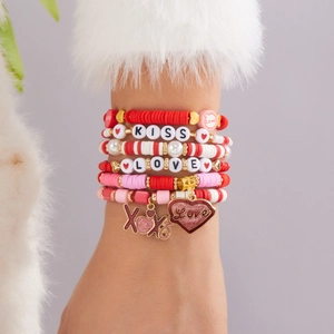 Détail de bracelets perlés roses et rouges avec lettrage KISS LOVE et breloque cœur pailleté
