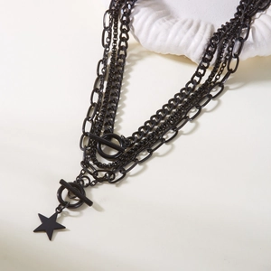 Close-up of layered matte black necklace with star pendant and decorative OT toggles