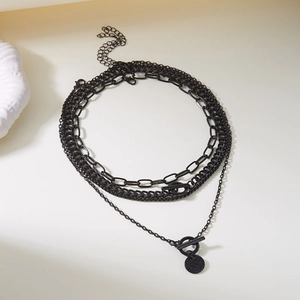Detail view of multi-layered black necklace featuring OT buckle and round charm pendant