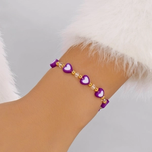 Dettaglio dei ciondoli a cuore viola e perle dorate su un bracciale di perline da donna