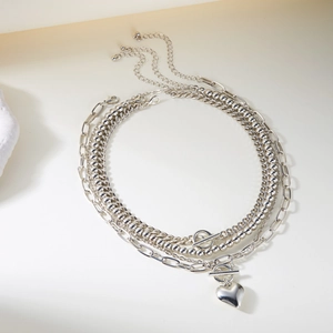Detail of layered silver necklaces with heart pendant and OT buckle on a minimalist stone