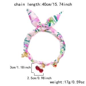 Detail eines rosa Stoff-Chokers mit Blumenmuster goldener Schleife und Kirsch-Anhängern