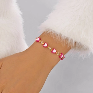 Dettaglio delle perline a cuore e accenti dorati sul braccialetto rosa indossato al polso