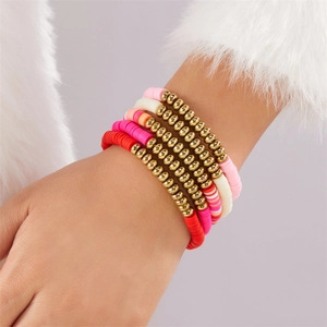 Nahaufnahme von fünf geschichteten Heishi-Armbändern mit rosa Herzanhängern am Model