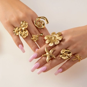 Detail showing golden ring set with starfish, flowers, and palm tree designs on a hand