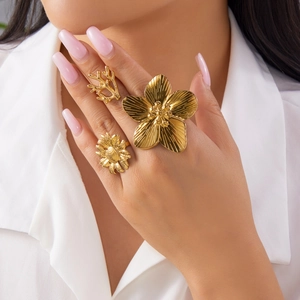 Detailed view of three gold flower and branch rings worn on model fingers