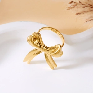 Macro detail of golden bow-shaped ring on a minimalist display with dry flowers