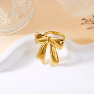 Detail shot of a golden bow-knot ring on a white wavy tray with warm soft lighting