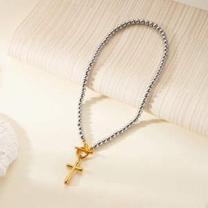 Close-up of golden cross pendant with OT toggle buckle on silver beaded necklace