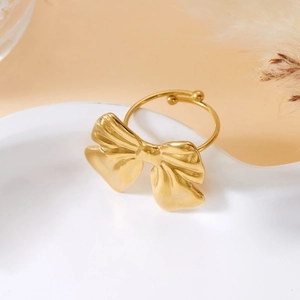 Detail of adjustable gold bow ring with textured metallic finish on a white plate