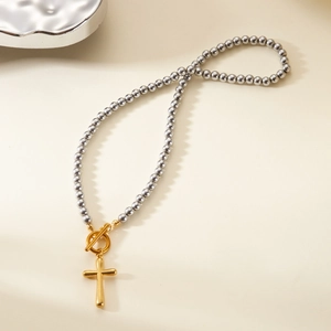 Detail view of a gold cross pendant on silver beaded necklace with toggle clasp