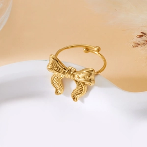 Detail of adjustable gold bow ring on a ceramic tray with a warm minimalist backdrop
