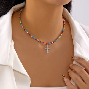 Colorful beaded necklace with a silver crystal-encrusted cross pendant on white shirt