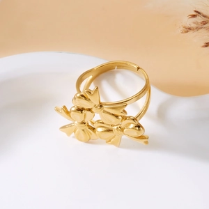 Detail shot of golden triple bow adjustable ring on a white ceramic tray with soft lighting
