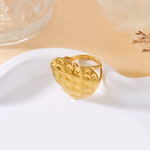 Macro shot of gold heart ring with hammered texture and relief dots on a ceramic plate