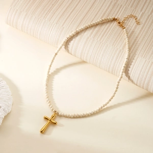 Detailed close-up of a gold cross pendant on a cream natural stone beaded necklace