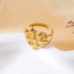 Detail of golden adjustable heart ring with embossed star patterns on white ceramic tray