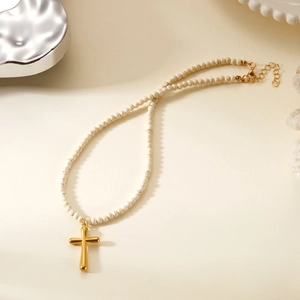Macro detail of golden cross pendant on white marble beaded necklace with gold lobster clasp
