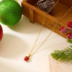 Détail d'un collier avec pendentif fraise doré sur un fond festif de décorations de Noël