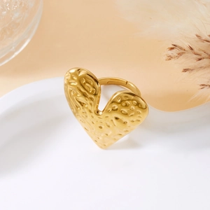 Detail of gold heart ring with hammered texture on a ceramic dish background