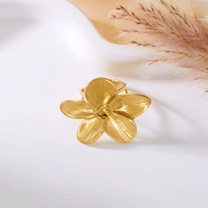 Macro view of gold plumeria flower ring with radial textures on a white ceramic dish