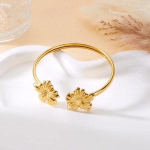Makro-Detail des goldenen Edelstahl-Armreifs mit filigranem, offenem Blumendesign