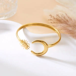 Detail eines goldenen Armreifs mit Sonnen- und Mondmotiven auf weißer Keramikschale
