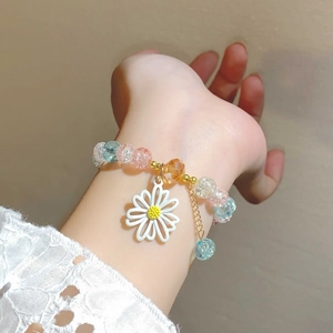Nahaufnahme eines Gänseblümchen-Anhängers an einem Armband mit hellblauen und rosa Perlen