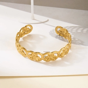 Detailed view of golden stainless steel cuff bracelet with hollow floral pattern