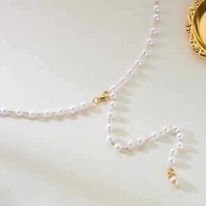 Détail de la chaîne de taille en perles blanches avec fermoir doré et pendentif brillant