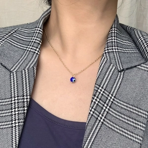 Gros plan d'un collier pendentif Mauvais Œil doré sur un modèle en blazer