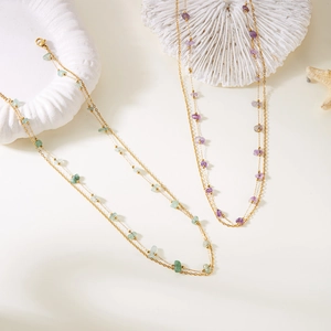 Detail of gold necklaces with purple and green natural stones on textured white props