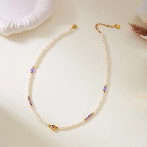 Detail of beaded necklace with white pearls, purple stones and golden heart pendant