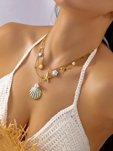 Detalle de collar dorado multicapa con colgante de concha azul y perla marina