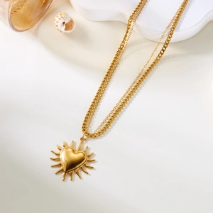 Detalle de collar dorado de doble capa con colgante de corazón 3D y rayos de sol