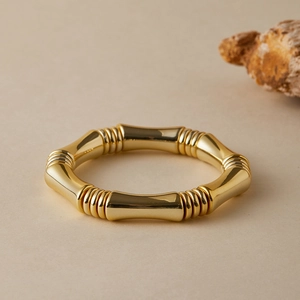 Dettaglio di un bracciale dorato con design a bambù su uno sfondo beige testurizzato