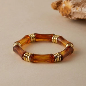Dettaglio del bracciale in resina ambrata con perle dorate e design a bambù