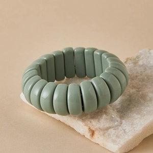 Macro view of a matte green beaded stretch bracelet on white stone textured background