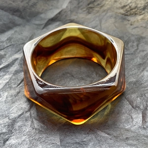 Dettaglio di un bracciale esagonale in resina ambrata con bordi lucidi su carta grigia